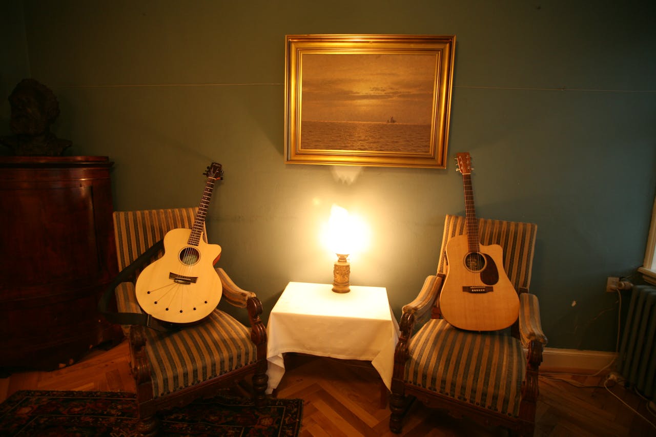services-03 Warm, inviting room with two acoustic guitars, a table lamp, and classic decor.